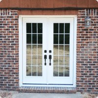 Modern white double French doors with glass panels installed on brick exterior, perfect for enhancing curb appeal and outdoor living spaces.