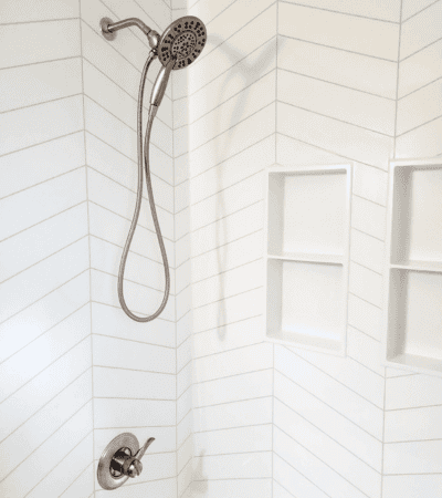 Modern shower with handheld detachable showerhead and built-in recessed shelves in a tiled bathroom.