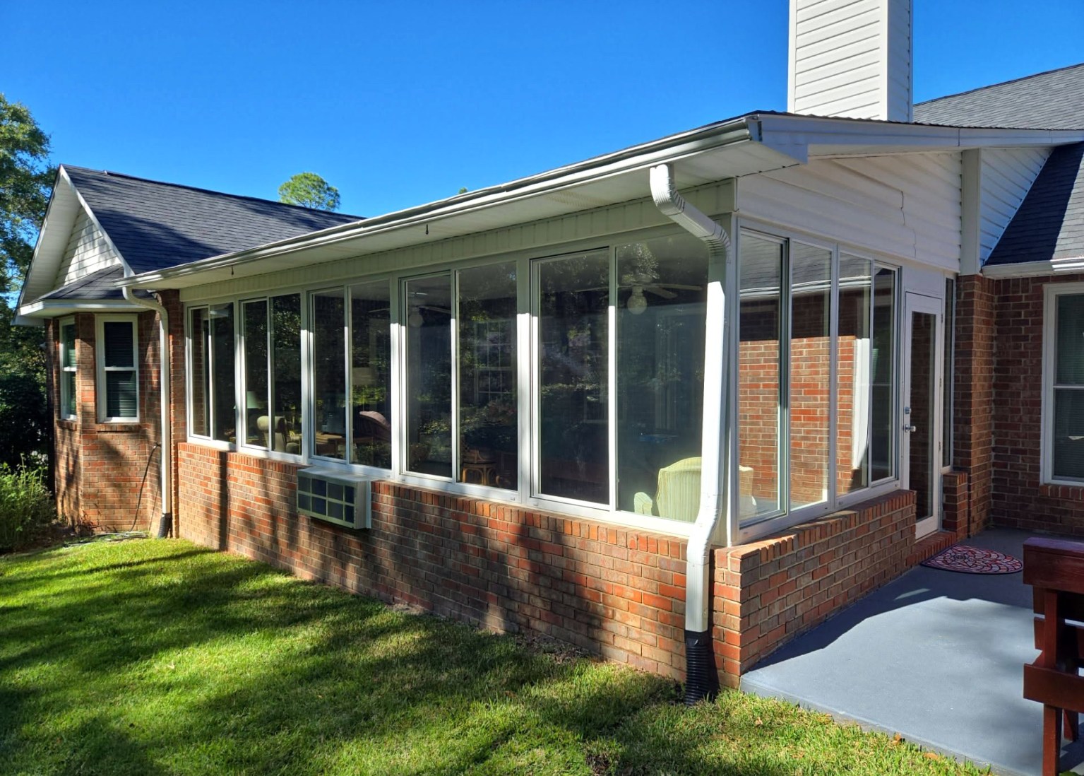 Gallery Glass Enclosure Brick Home Angled view of a porch glass enclosure from the outside with one white glass door on the side.
