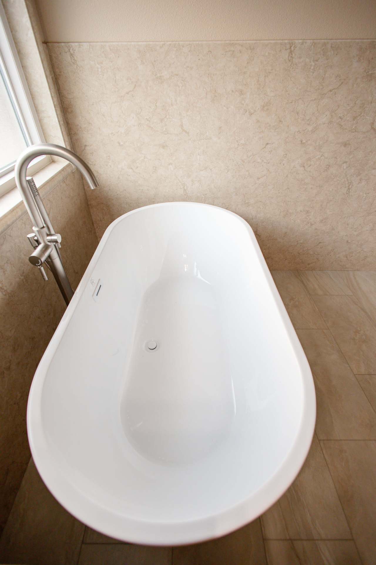 Gallery Standalone Tub Close angle of white standalone bathtub with a tall silver faucet and beige walls