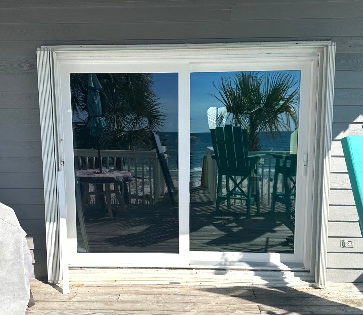 Gallery Wide Sliding Glass Door Outside view of sliding glass doors with reflection of a wooden balcony leading to the beach.