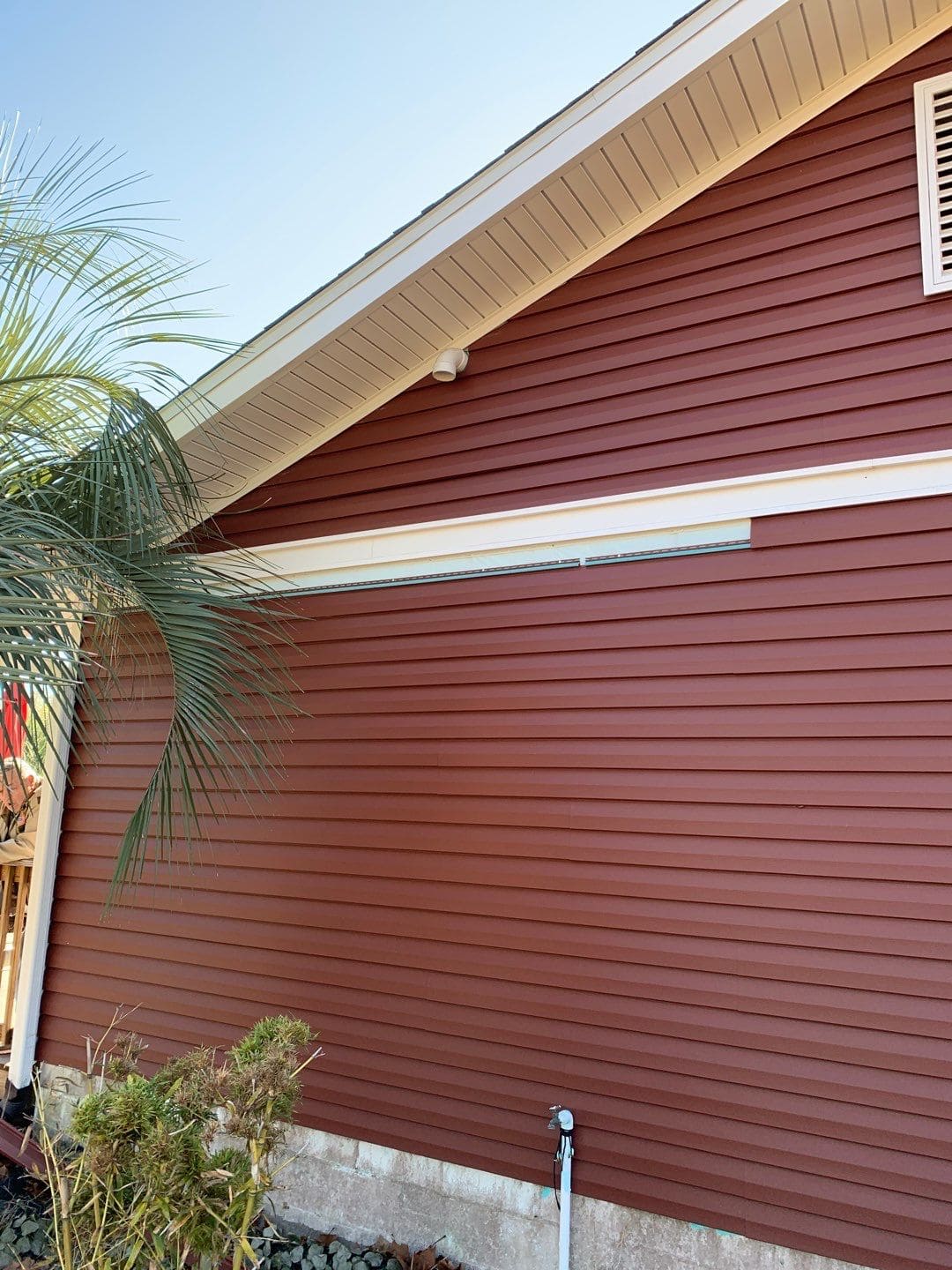 Gallery Fired Brick Siding Dark red vinyl siding with white soffits and fascia and branches of a palm tree visible on the left