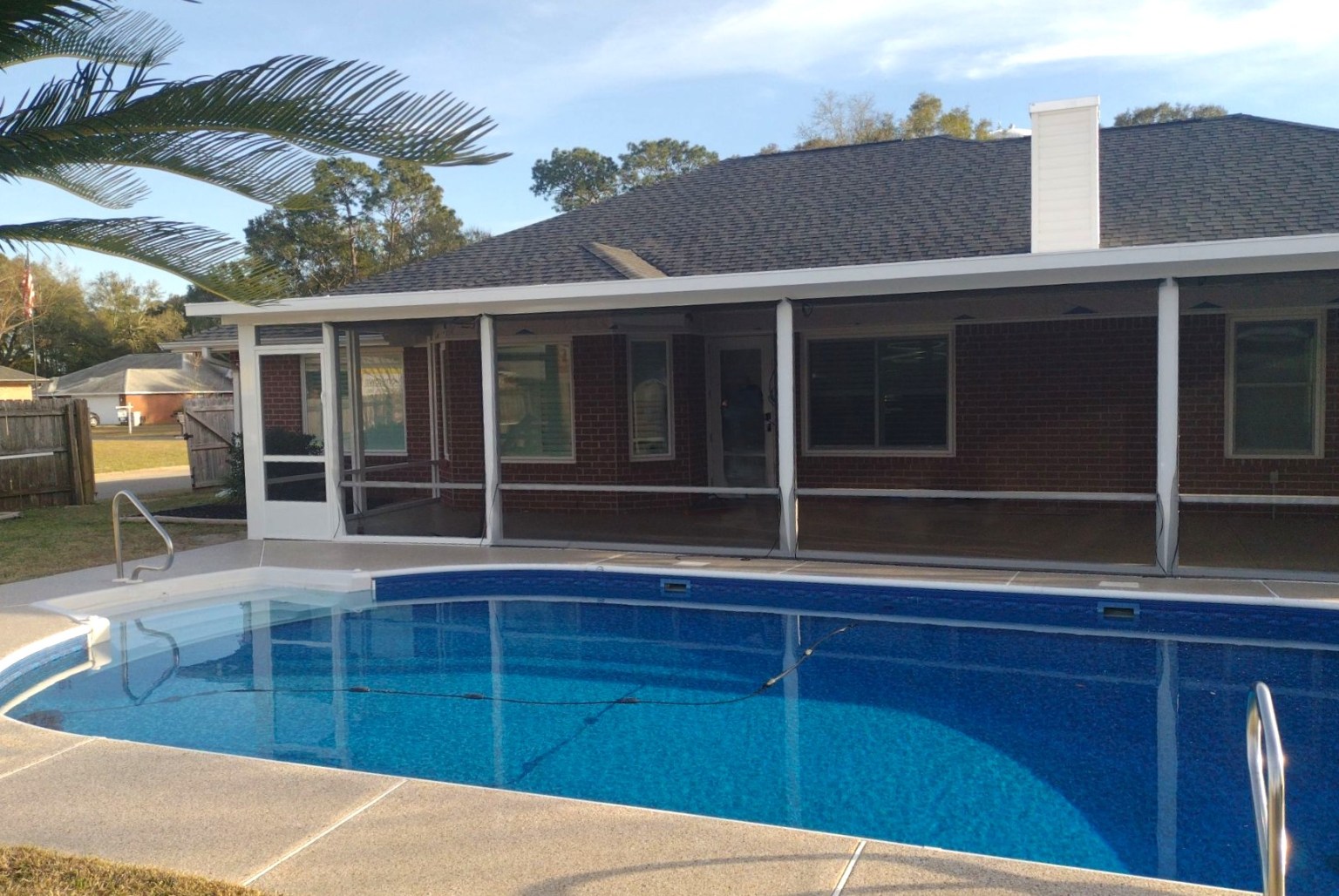 Gallery Screen Room Behind Pool1 White-trimmed screen room at an angle attached to a brick home with a pool outside