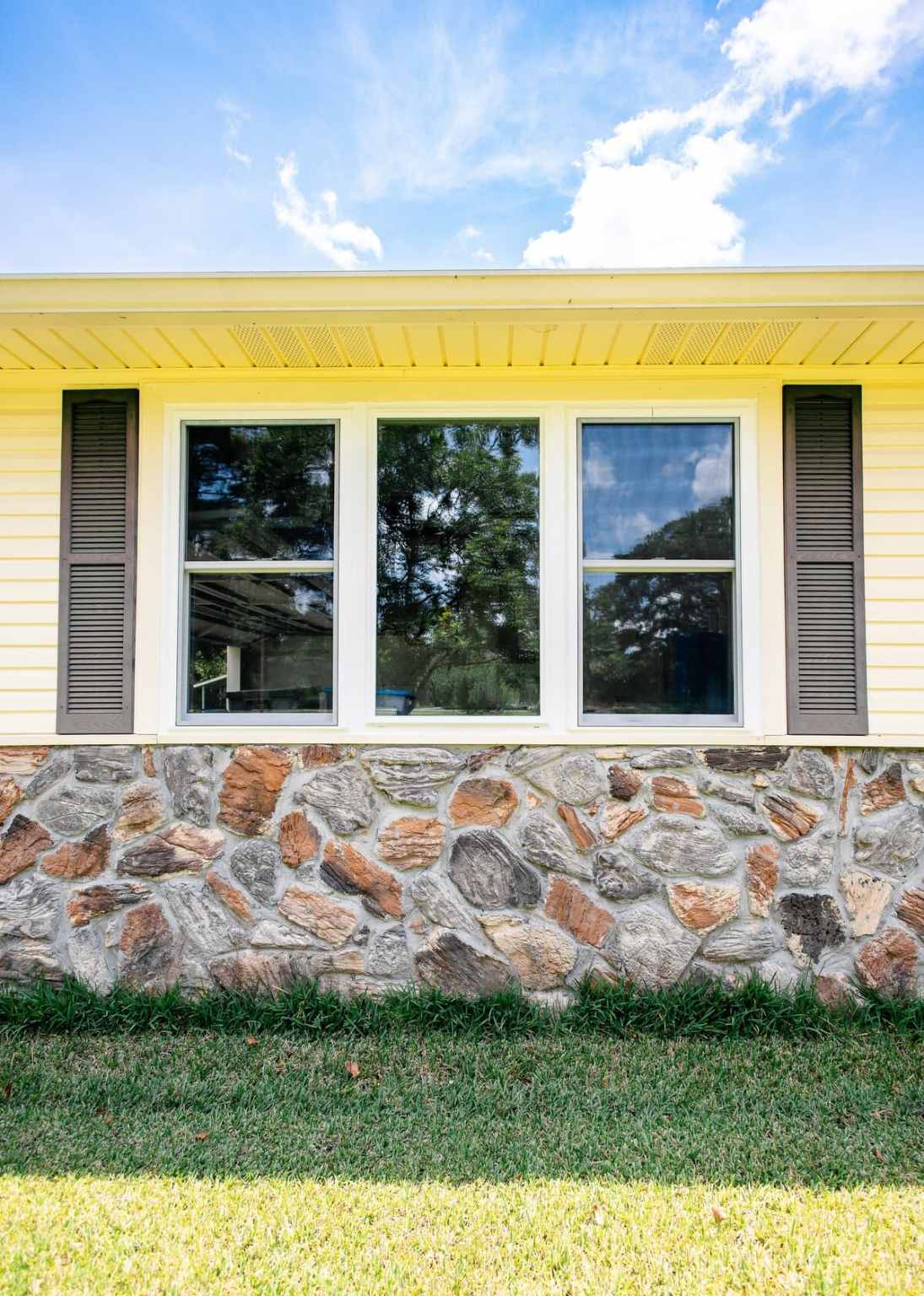 Three Impact Windows Three impact windows with brown shutters and a stone-like pattern below on the side of the home