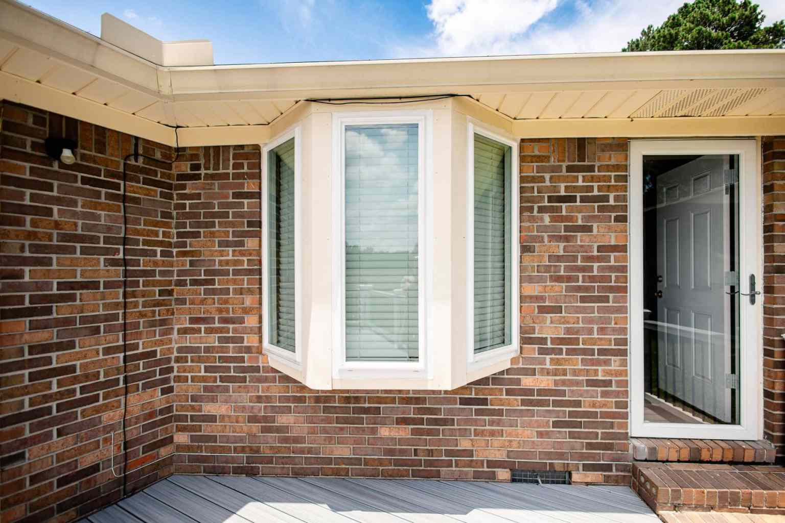 Three Picture Windows Three vertical picture windows with white trimming attached to the side of a brick home