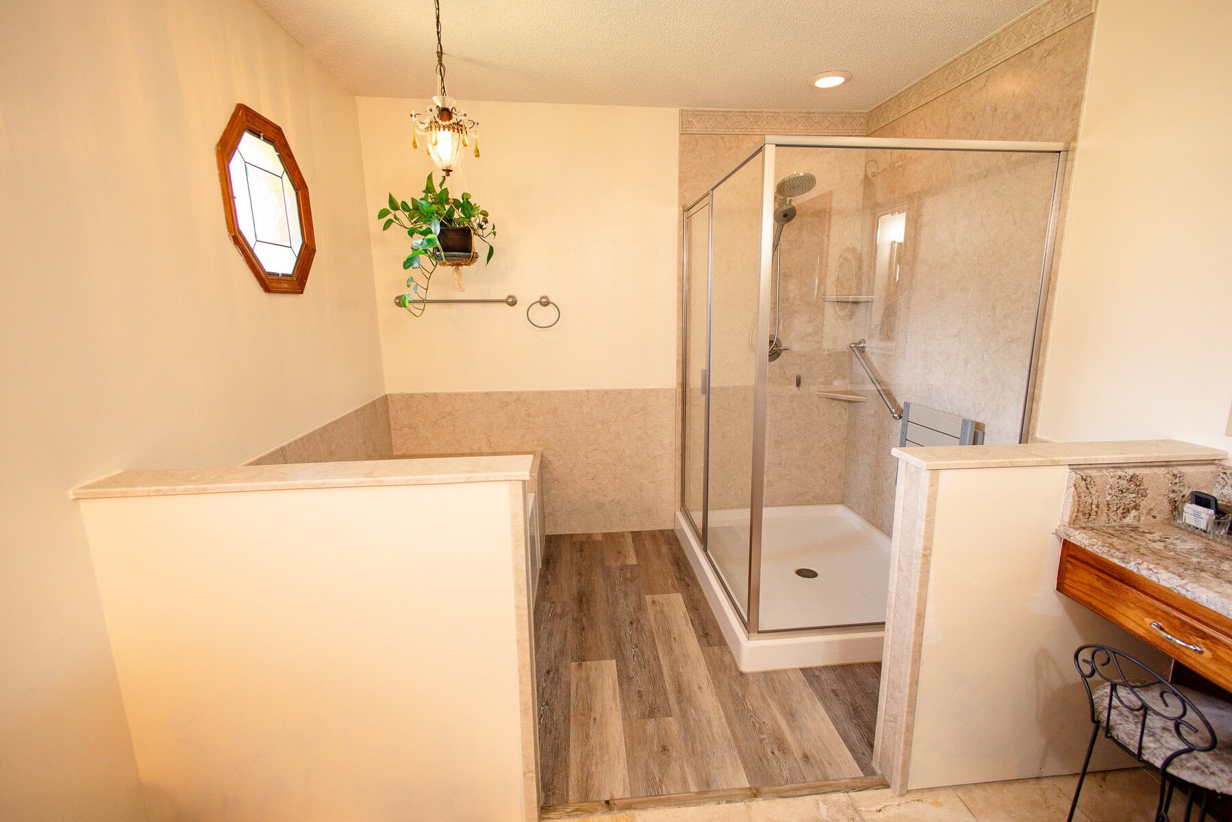 Entire bathroom with glass-enclosed shower and beige walls behind two knee walls