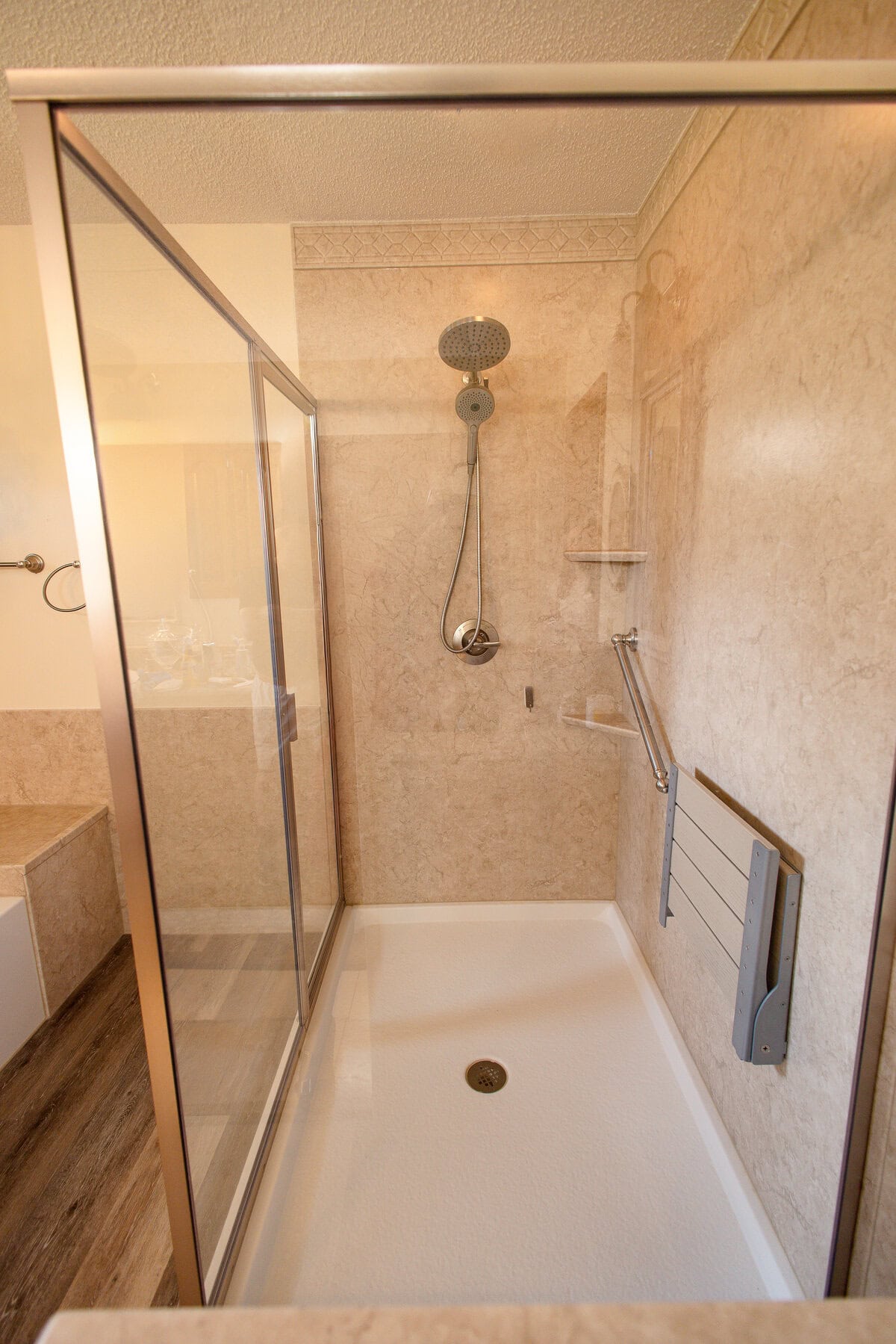 LatashaCarrawayPhotography-8540copy Up close angle of glass-enclosed shower with beige wall surrounds, silver hardware, and beige fold-down seat on the right