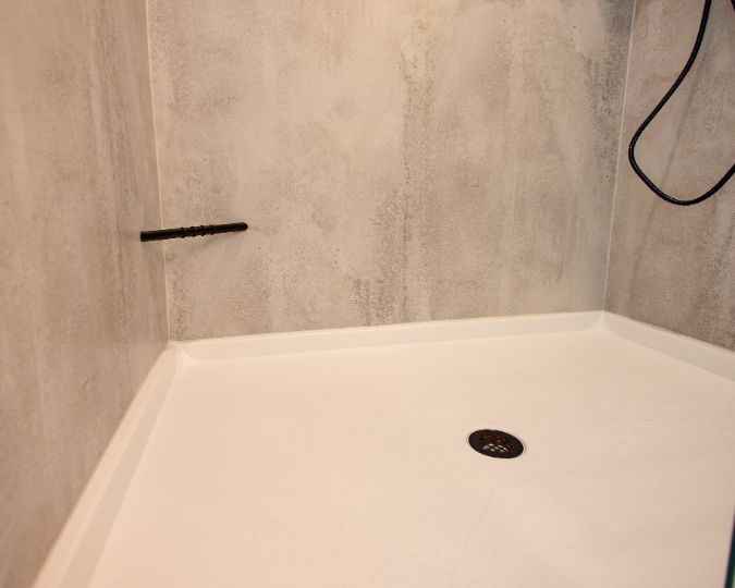 White shower pan with black drain and black shave bar attached to concrete-like shower walls