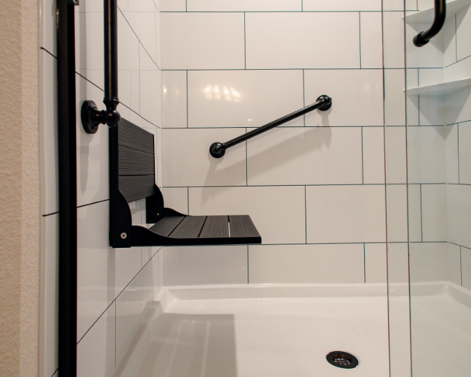 Dark fold-down seat in a white shower with black grab bar to the side