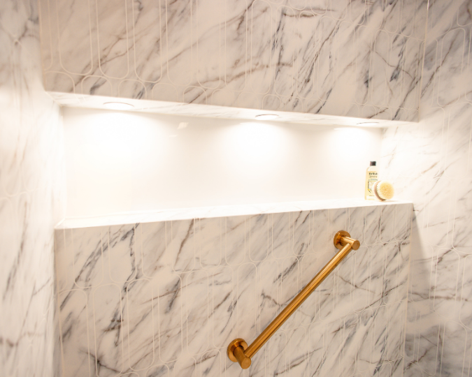 Gold grab bar attached to white and gray marbled shower with rectangle cut-out shelf
