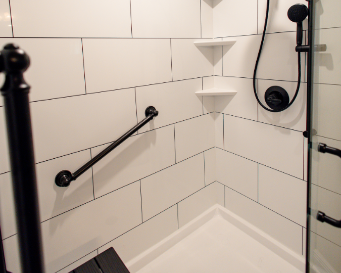 Black grab bar attached to white and black tile-like shower walls