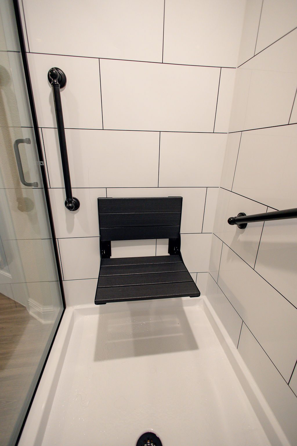 LatashaCarrawayPhotographyAFTER-8642 Walk-in shower with black wooden fold-down seat, grab bar, and white drain pan.