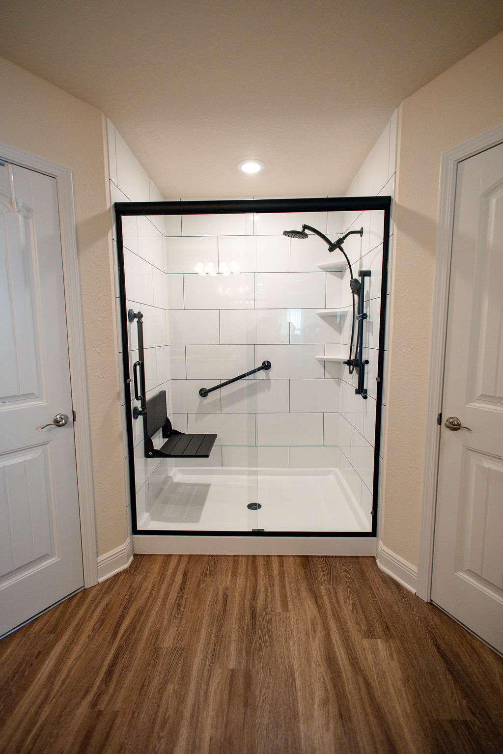LatashaCarrawayPhotographyAFTER-8649 New walk-in shower installed by Hometown Contractors, featuring white subway tile surrounds, black fold-down seat, grab bar, and corner shelving.