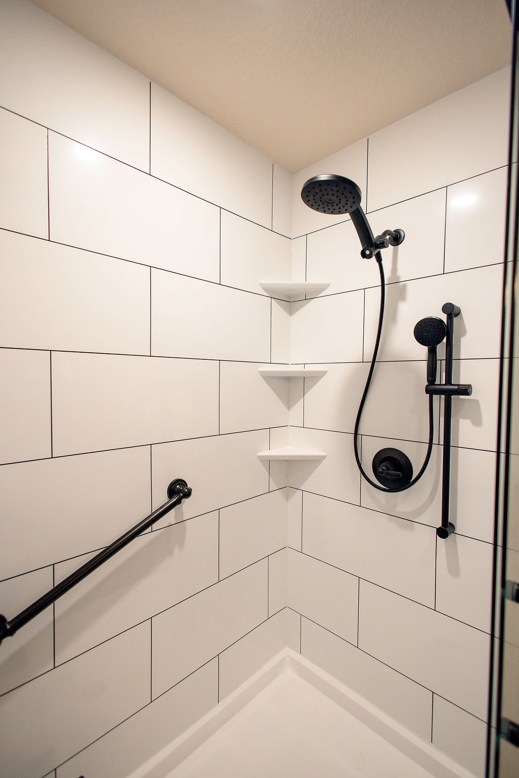 LatashaCarrawayPhotographyAFTER-8659 white subway tile style walk-in shower, with detachable wand, corner shelves, and grab bar.